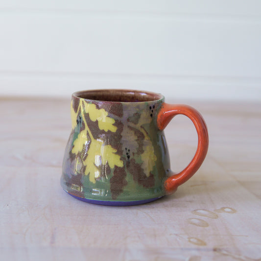 Ceramic mug with floral design and orange handle on a painterly surface